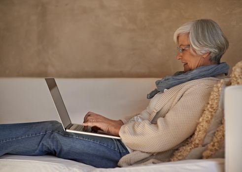 Enjoying a bit of web browsing. A happy senior woman working on her laptop at home.