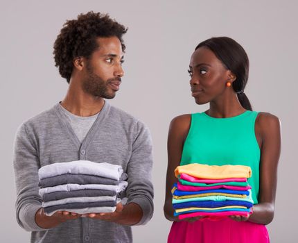 Fashion faceoff. Studio shot of a young man and woman each holding a neatly folded pile of clothes.