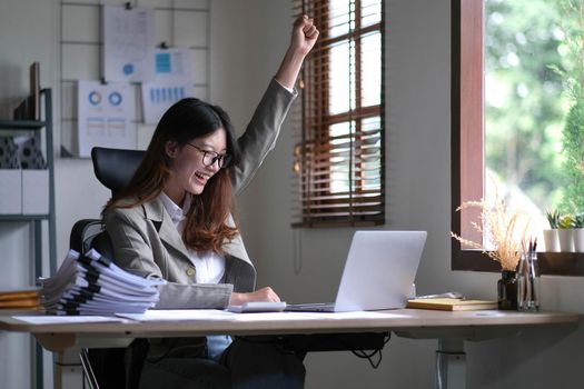 young Asian businesswomen successful excited raised hands rejoicing with a laptop computer in a modern office.