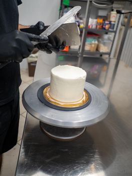 Decorator using spatula and scraper to smooth buttercream on a frosted cake