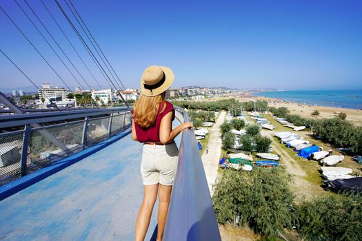 Beautiful young woman on modern bridge enjoying Pescara seascape from promenade in Abruzzo region, Italy