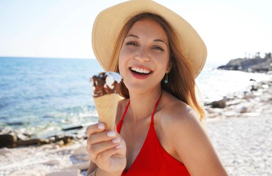 Close-up of beautiful bikini woman with hat holding eating ice cream cone italian gelato on the beach on summer