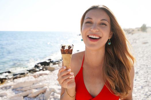 Beautiful young woman smiling with ice cream cone looking at camera on beach