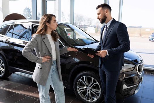 a young woman in a car dealership is interested in the details of the contract when buying a new car