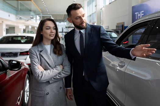 car dealership representative presenting a new car to a young woman buyer