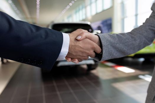 handshake against the backdrop of a car dealership at a deal, the concept of buying a car on lease