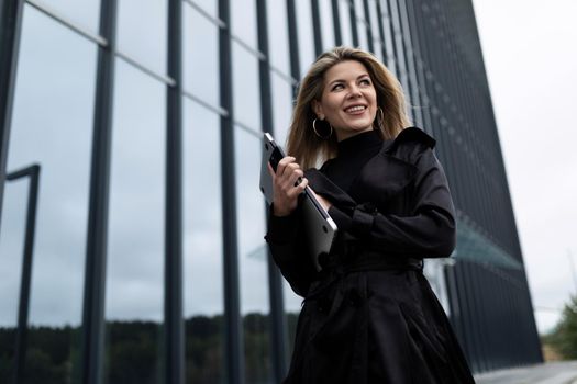 portrait of a successful business woman with a laptop in her hands against the backdrop of an office skyscraper