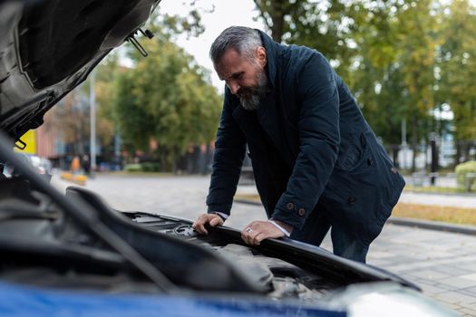 mature man trying to figure out a car breakdown leaning over the engine in the city