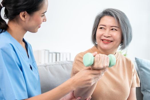 Caregiver helping contented senior woman exercise with dumbbell at home.