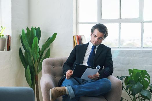 Young businessman reading paperwork, on couch at home and looking at financial analysis document for career development. Business finance report, changes in economy and success with accounting audit