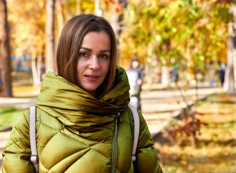 Charming young woman in a green jacket among colorful golden autumn foliage