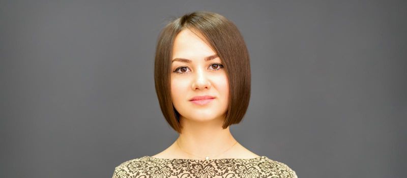 Beautiful young caucasian brunette woman with short hairstyle smiling and looking at camera against dark gray background with copy space.