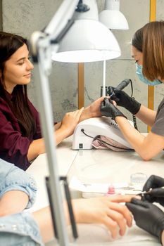 Manicure master in rubber gloves applies an electric nail file to remove the nail polish in a nail salon.