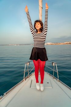 Woman standing on the nose of the yacht at a sunny summer day, breeze developing hair, beautiful sea on background