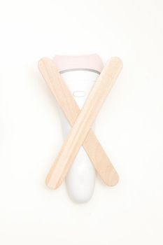 Waxing, depilation concept. Flat lay of the white epilator with wooden sticks lying on white background.
