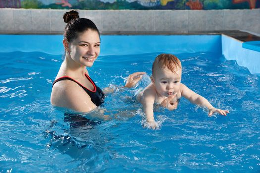 Little baby learning to swim in pool with teacher
