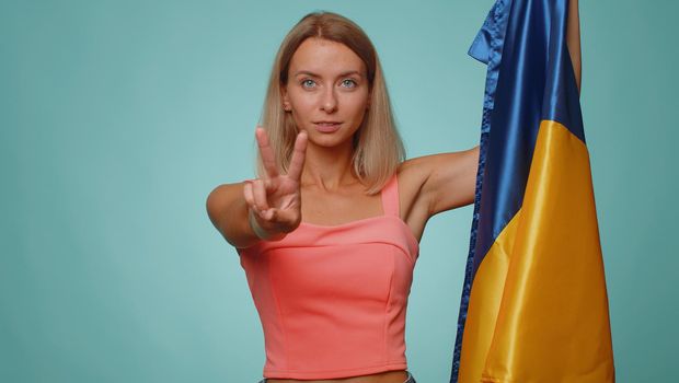 Woman holding Ukraine national flag, showing victory sign against war, hoping for success and win