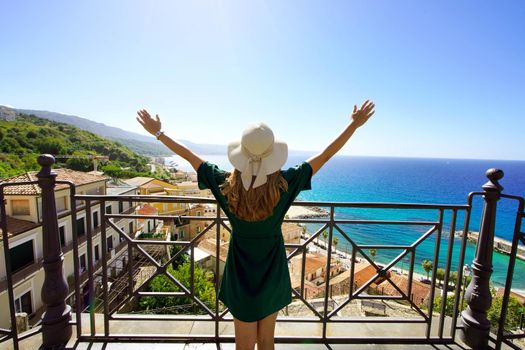 Amazing panoramic view from a terrace in Italy. Tourist girl happy outstretched arms enjoying life. Traveler woman raising hands in Pizzo, Calabria, Italy.