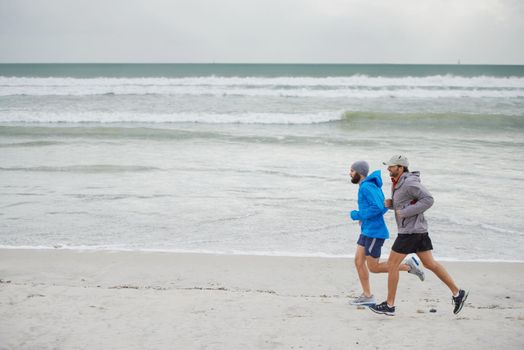Keeping up with a friend. Full length shot of two men jogging together along the beach on an overcast morning.