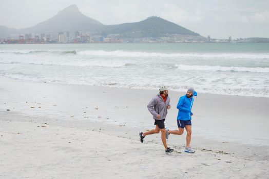 Motivated by the scenic vista. Full length shot of two men jogging together along the beach on an overcast morning.
