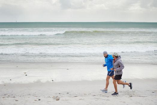 Admiring the sea as runners pass by. Full length shot of two men jogging together along the beach on an overcast morning.