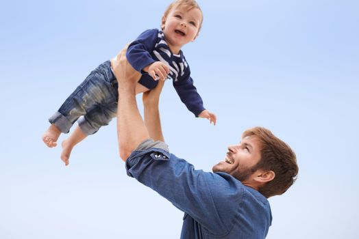 He only has eyes for his boy. a young man lifting his son up into the air.
