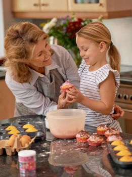 That looks delicious. a little girl decorating cupcakes with the help of her grandmother.