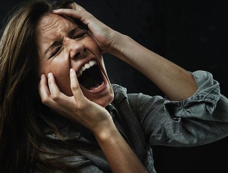 Someone please help. A young woman screaming uncontrollably while isolated on a black background.