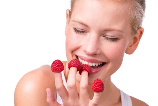 Tasty tips. a beautiful young woman playfully eating raspberries off her fingertips.