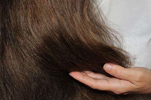 A girl with long dark hair holds curls in her hand. Hair care. Hair loss problem