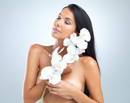 Beauty is more than skin deep. Cropped studio shot of a beautiful woman holding a flower against her body.