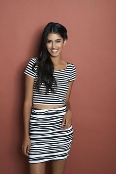Shes got a dazzling smile. Studio shot of a beautiful young Indian woman standing against a brown background in casual attire.