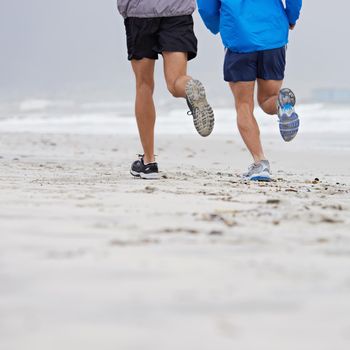 Getting some serious training done. two unrecognizable men jogging together along the beach on an overcast morning.