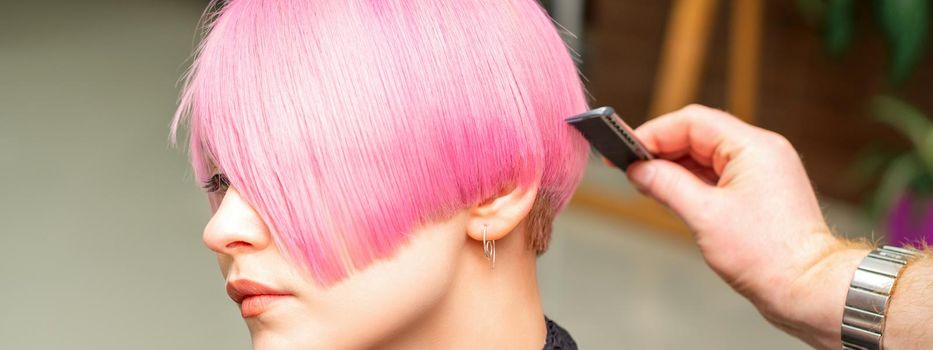 A hairdresser is combing the dyed pink short hair of the female client in a hairdresser salon.