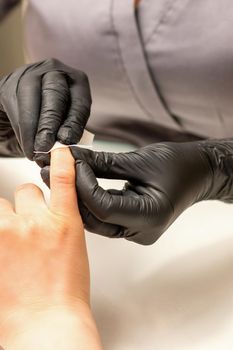 The manicurist finishes the procedure for red nail polishing and cleaning with a cotton napkin, pad, swab in a beauty salon, close up.