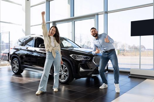 satisfied young couple dancing next to a new purchased car from a car dealership