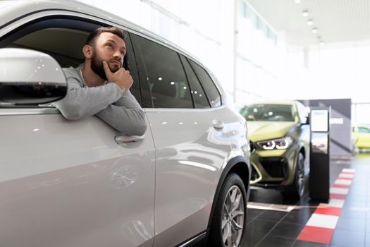 a buyer in a car dealership sits in an SUV and thinks about buying and insuring a new car