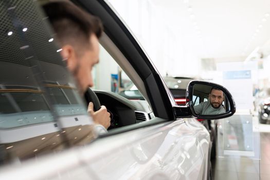 a man at a car dealership driving a car looks in the rearview mirror