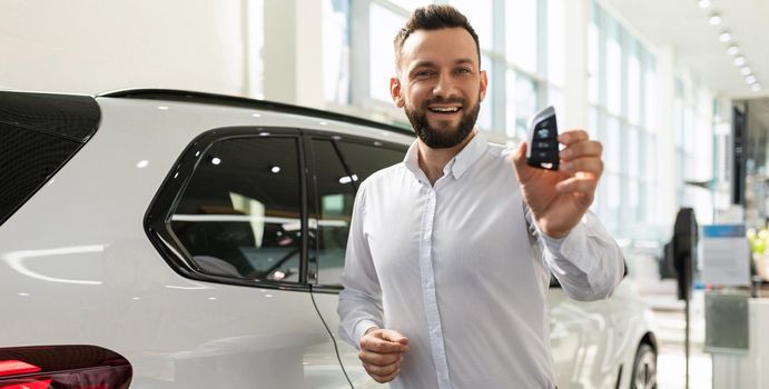 satisfied buyer of a new prestigious SUV with a key in hand in a car dealership