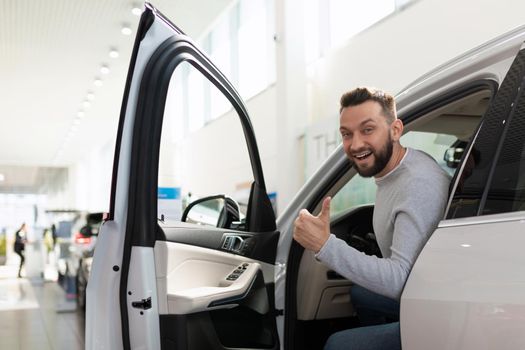 joyful man in a car dealership with a smile on his face in a new SUV
