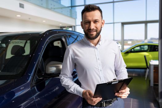 charming salesman in a car dealership against the background of new premium cars
