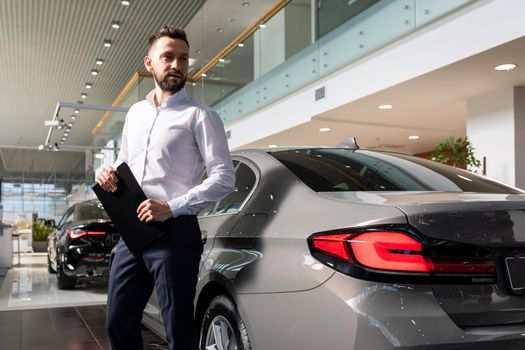 successful manager in the showroom of a car dealership with a tablet in his hands