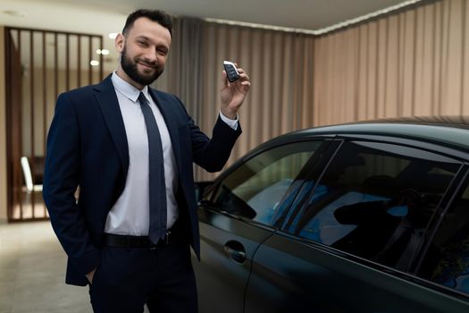 satisfied businessman with a key to a prestigious car in a car dealership