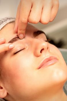 Eyebrow massage. Beautiful caucasian young white woman receiving an eye and eyebrow massage with closed eyes in a spa salon.