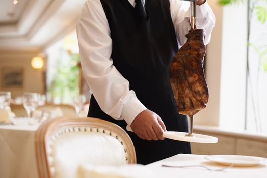 That looks delicious. Cropped image of a male waiter holding a skewer with a large piece of meat on it.