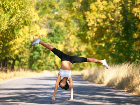 Filled with energy. A young woman doing a cartwheel in the middle of the road.