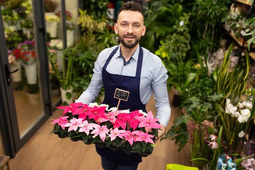 botanist against the background of the garden center with a tray of potted plants in his hands