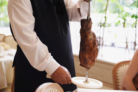 That looks delicious. Cropped image of a male waiter holding a large piece of meat on a stake.
