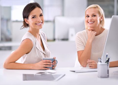 Enjoying their coffee break together. Two businesswomen sitting together at a desk.
