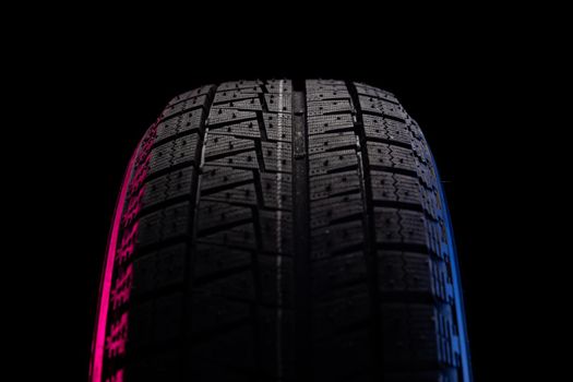 black tire with tread for driving on snow on a black background with blue red illumination